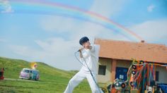 a man in white pants holding a microphone while standing next to a rainbow colored house