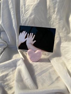 two hands reaching for a pink heart on a white sheet with black border around it