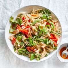 a white bowl filled with pasta salad next to a cup of sauce on a table