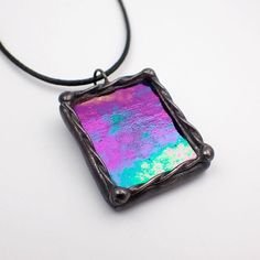 a square necklace with a purple and green holographic design on it's back