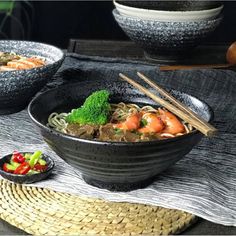 a bowl of noodles with chopsticks and broccoli on the side next to another bowl