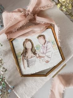 an embroidered picture frame with a pink ribbon tied around it and flowers in the background