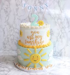 two tiered cake decorated with sun and clouds on marble countertop next to white wall