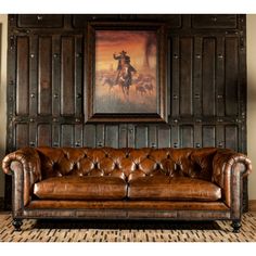 a leather couch sitting in front of a wooden paneled wall with a painting on it