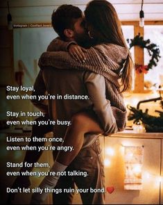 a man and woman hugging each other in front of a kitchen counter with christmas lights