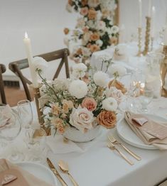 the table is set with white and pink flowers, gold cutlery, and candles