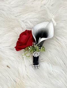 a white and black vase with a red rose in it sitting on a fur surface