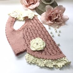 two crocheted sweaters with flowers and pearls on the bottom one is pink