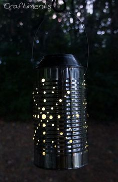 a tin can with lights on it hanging from the side of a tree branch in front of some trees