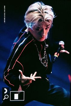 a man with blonde hair holding a microphone in one hand and making the peace sign