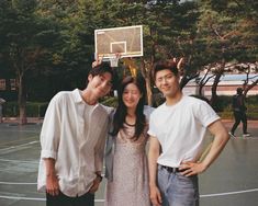 three people standing on a basketball court posing for a photo with the hoop in the background