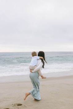 a woman carrying a baby on the beach