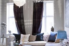 a living room filled with lots of furniture next to a window covered in purple drapes