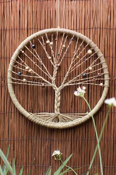 a wicker wall hanging with a tree on it and flowers in the foreground