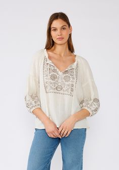 [Color: Natural/Taupe] A front facing image of a brunette model wearing an ivory flowy bohemian peasant top with embroidered detail and tassel ties. Spring Folk Style V-neck Peasant Top, Bohemian V-neck Peasant Top With Boho Print, Bohemian V-neck Blouse With Tassels, Fall Bohemian Split Neck Tops, Bohemian V-neck Blouse With Embroidered Hem, V-neck Peasant Top With Boho Print, Summer Embroidered V-neck Peasant Top, Bohemian V-neck Blouse With Boho Collar, Traditional V-neck Spring Blouse