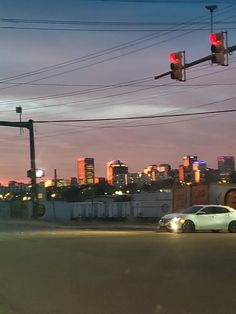 a car is stopped at an intersection in front of a city skyline as the sun sets