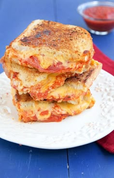 two grilled cheese sandwiches stacked on top of each other with tomato sauce in the background