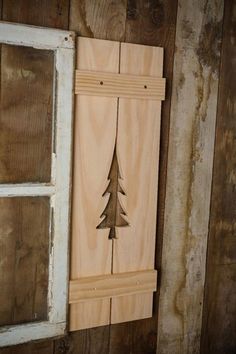 a wooden wall hanging with a pine tree cut out on it's side and an open window in the background