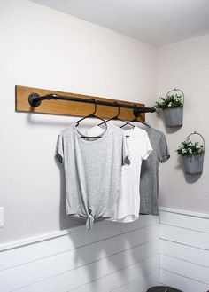 two t - shirts hanging on a clothes rack in the corner of a white room