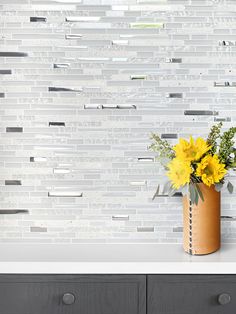 a vase with yellow flowers sitting on top of a counter next to a white tiled wall