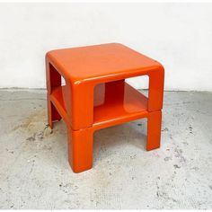 an orange plastic stool sitting on top of a cement floor next to a white wall