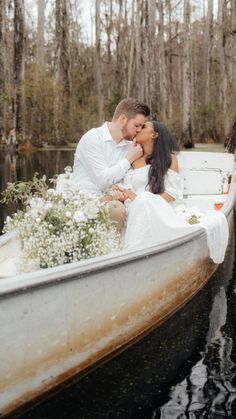 a man and woman are kissing in a row boat on the water, surrounded by trees