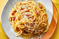 a plate of spaghetti with bacon and parmesan cheese on top, sitting on a yellow tablecloth