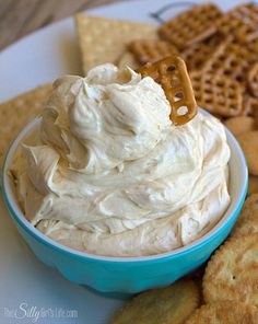 a blue bowl filled with whipped cream surrounded by crackers and pretzel sticks