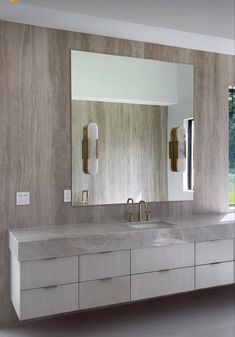 a bathroom vanity with two sinks and mirrors on the wall above it, in front of a large window