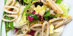 a salad with noodles, lettuce and olives on it is shown here