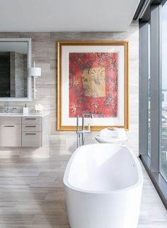 a large bath tub sitting in a bathroom next to a painting on the wall above it