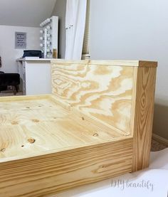 a bed frame made out of plywood is shown in the foreground with a woman sitting on a chair in the background