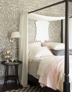 a white bed sitting in a bedroom next to a night stand with a lamp on top of it