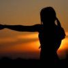 the silhouette of a woman with her arms outstretched in front of an orange and blue sky