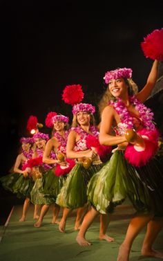 a group of women dressed in hula skirts and flower leis dancing on stage