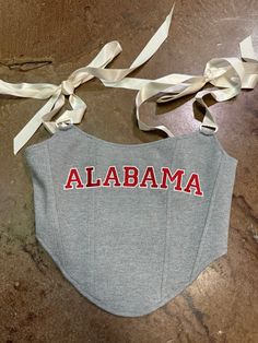 show your school spirit + fashion sense with our Alabama Crimson Tide ribbon corset top:: available in heather gray with an embroidered graphic on the front in Bama's iconic crimson flame! this tailgate top is a cropped bustier with boning at front + self tie satin shoulder straps for a girly touch! roll tide!! shop our game day collection here! details & care details self: 65% cotton, 30% nylon, 5% spandex lining: 100% polyester care hand wash only in cold water lay flat to dry no bleach Fitted Red Tops For Cheerleading, Red Fitted Tops For Cheerleading, College Outfits Game Day, Game Day Fits, Ribbon Corset, College Wear, Dressy Pants, Everyday Gifts, Belt Purse