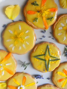 several decorated cookies on a white plate with flowers and leaves in the middle one has an orange star