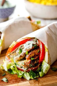 a sandwich with meat, lettuce and tomatoes on it sitting on a cutting board