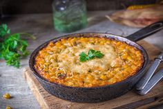 a casserole dish is sitting on a cutting board with silverware next to it