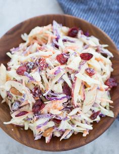 a wooden bowl filled with coleslaw and dried cranberries on top of a table