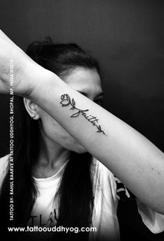 a woman is holding her arm up to the side with a flower tattoo on it