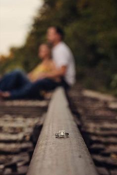 two people sitting on train tracks next to each other with their engagement rings in front of them