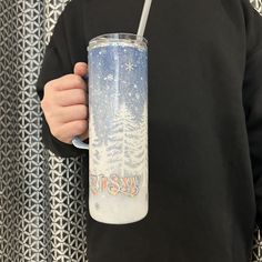 a person wearing a black sweatshirt holding a blue and white tumbler with trees on it