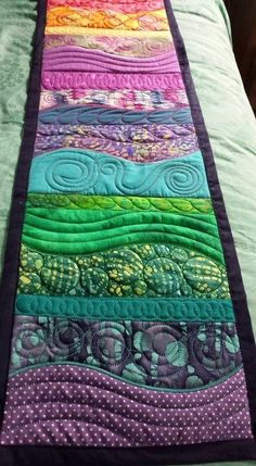 a quilted table runner made with different colors and patterns on the edge of a bed