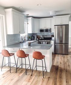 three bar stools sit at the center of a kitchen island with stainless steel appliances