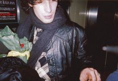 a young man wearing a black jacket and scarf is holding a banana in his hand