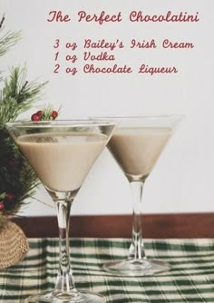 two martini glasses sitting on top of a checkered table cloth next to a pine tree