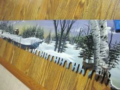 a wooden table topped with a painting of trees and animals in the snow covered forest