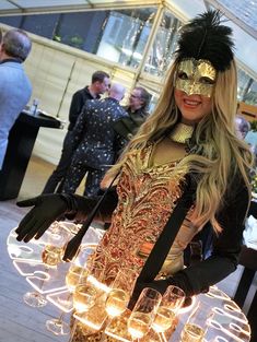 a woman wearing a mask and holding glasses in front of a table full of wine glasses