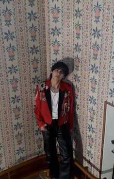 a young man standing in front of a wallpapered room with a red jacket on